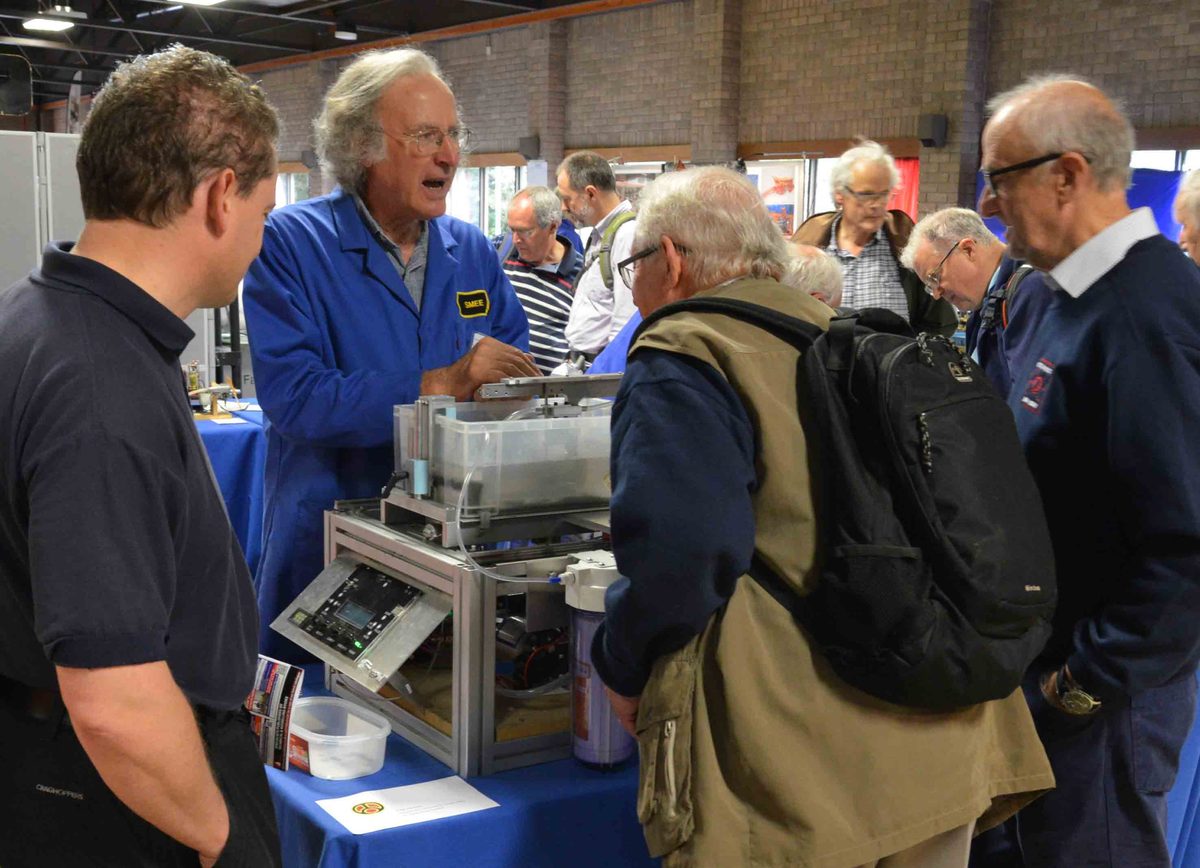A SMEE member in a blue coat demonstrating a model to visitors at the Bristol model engineering exhibition