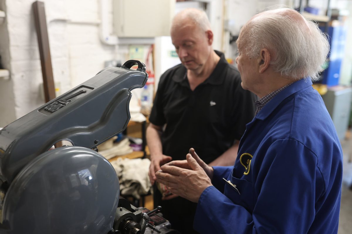 Two SMEE members, one in the blue Society coat, at a machine in the basement workshop